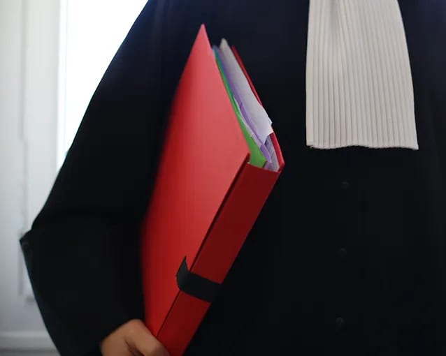 Un avocat en toge et rabat tient un dossier rouge