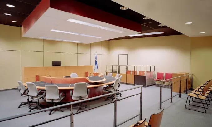 Une salle d’audience vide : le banc du juge, le drapeau du Québec et les sièges des parties